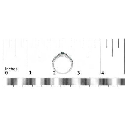 White metal ring with a single round blue gemstone center, flanked by multiple smaller round blue and white gemstones along the band, prong settings, positioned upright on a ruler for size reference, front angle.