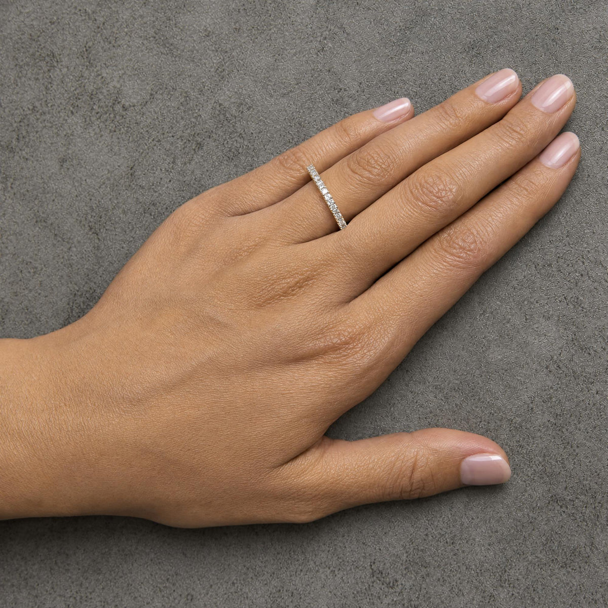 Yellow metal ring with princess shape white gemstones in prong setting, shown worn on a model’s hand, top down angle.