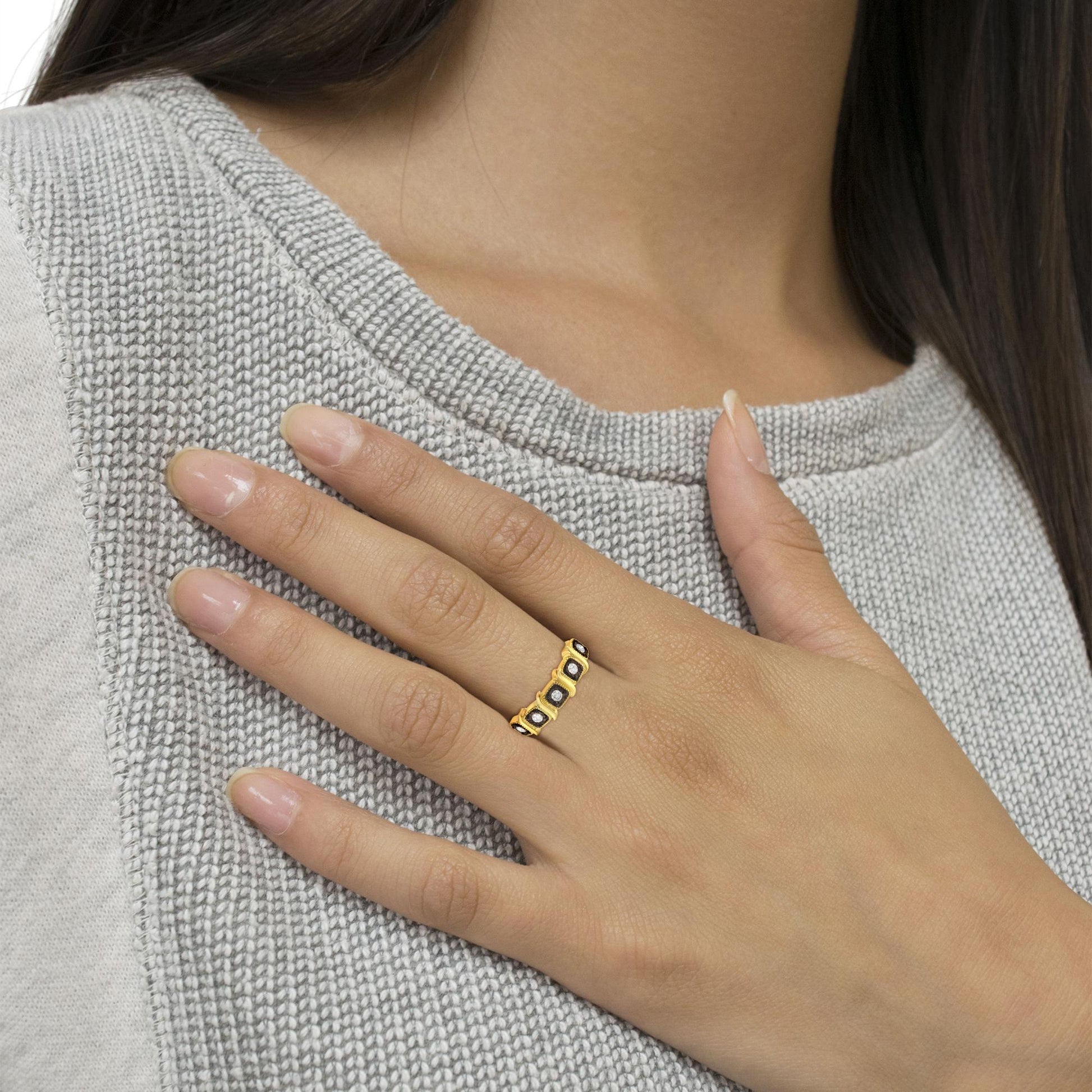 Close-up of a yellow and black metal ring with round white gemstones in miracle setting, worn on a model’s hand from a side angle.
