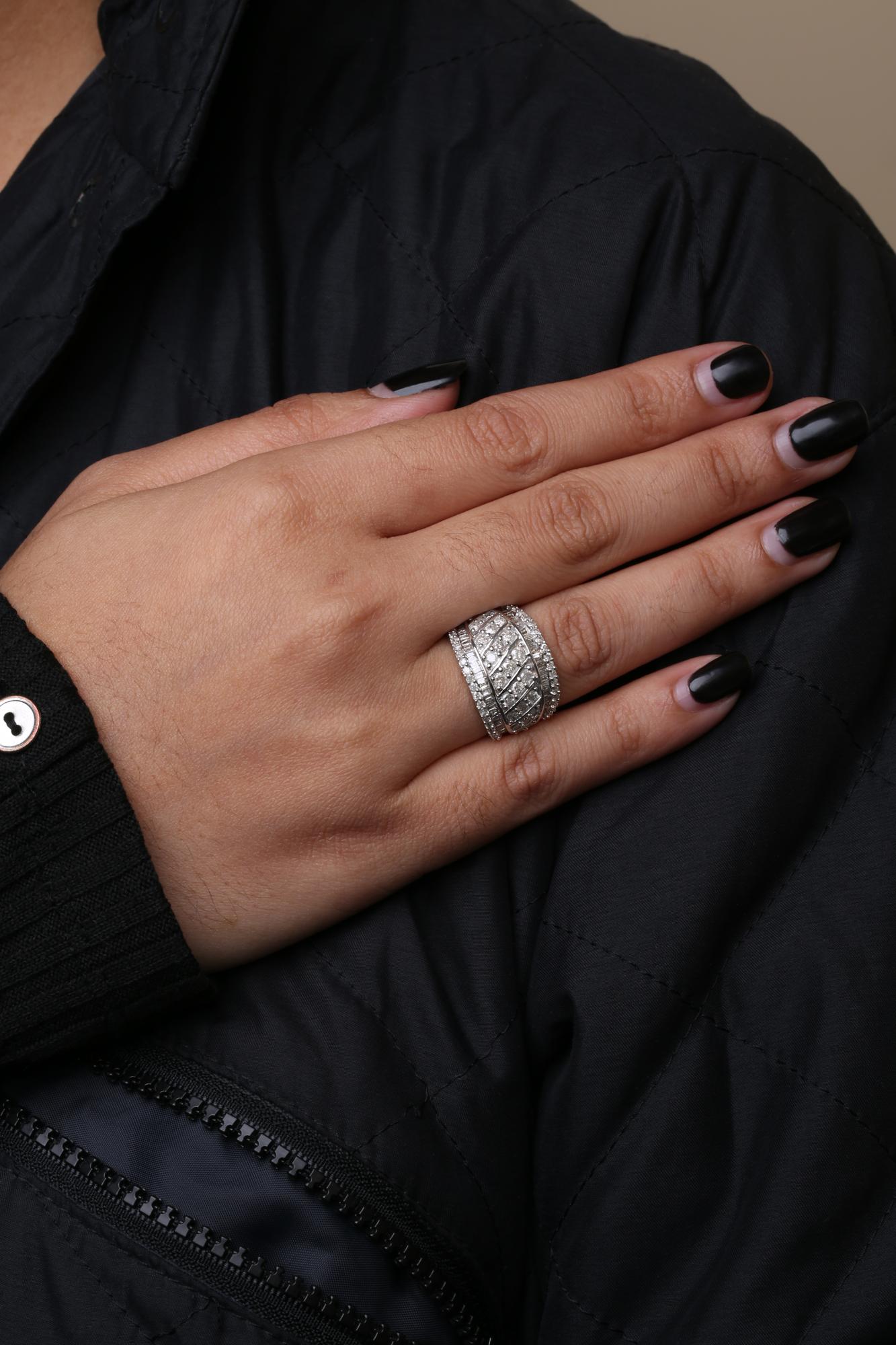 Close-up of a hand on a black jacket wearing a white metal ring with round prong-set white gemstones and baguette channel-set white gemstones, shown from a side angle.