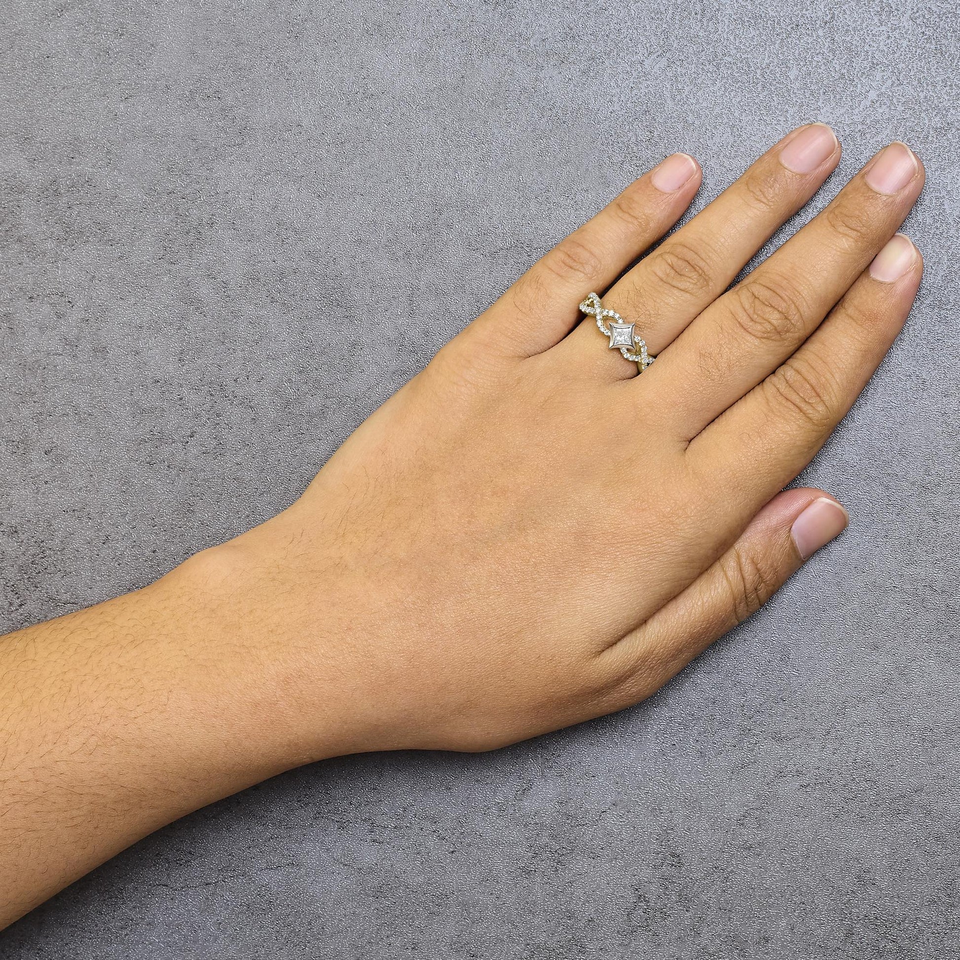 Ring with yellow and white metal featuring a princess-shaped white gemstone in a channel setting and multiple round white gemstones in prong settings, worn on a model's hand, photographed from above.