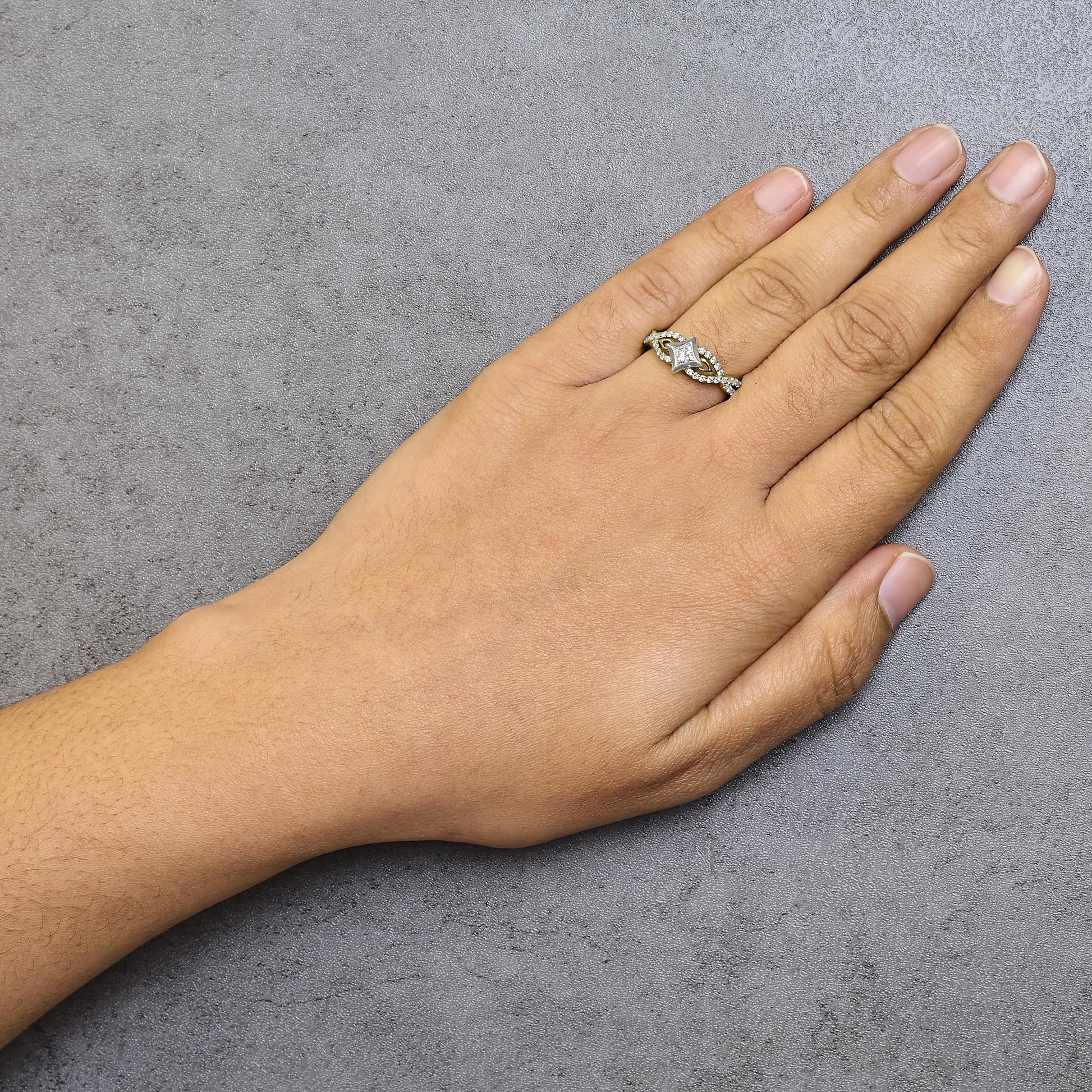 Yellow and white metal ring with a princess-shaped white gemstone in channel setting and multiple round white gemstones in prong settings, worn on a hand, top view angle.