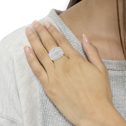 Close-up of a white metal ring with round and baguette-shaped white gemstones in prong and channel settings, worn on a model's hand positioned near the shoulder, angled slightly from above.
