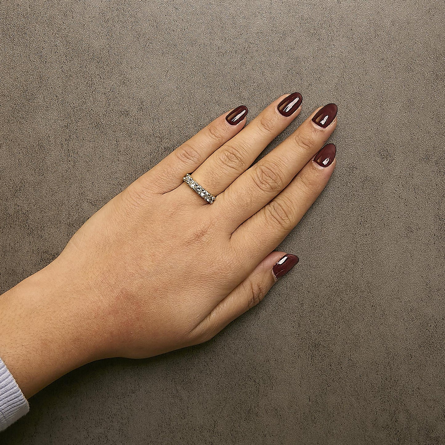 Top view of a hand wearing a yellow metal ring with round white gemstones in prong settings encircling the band.