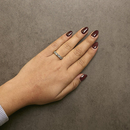 Top view of a hand wearing a yellow metal ring with round white gemstones in prong settings encircling the band.