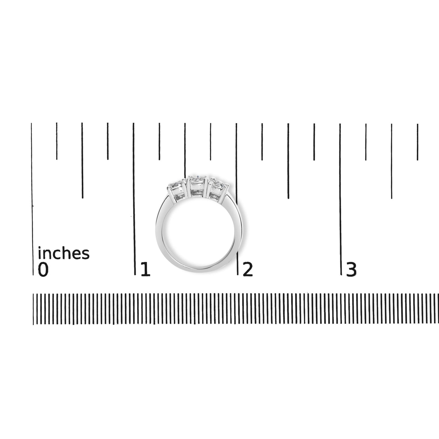 Top view of a white metal ring with three round white gemstones in miracle settings, placed on a ruler for size reference.