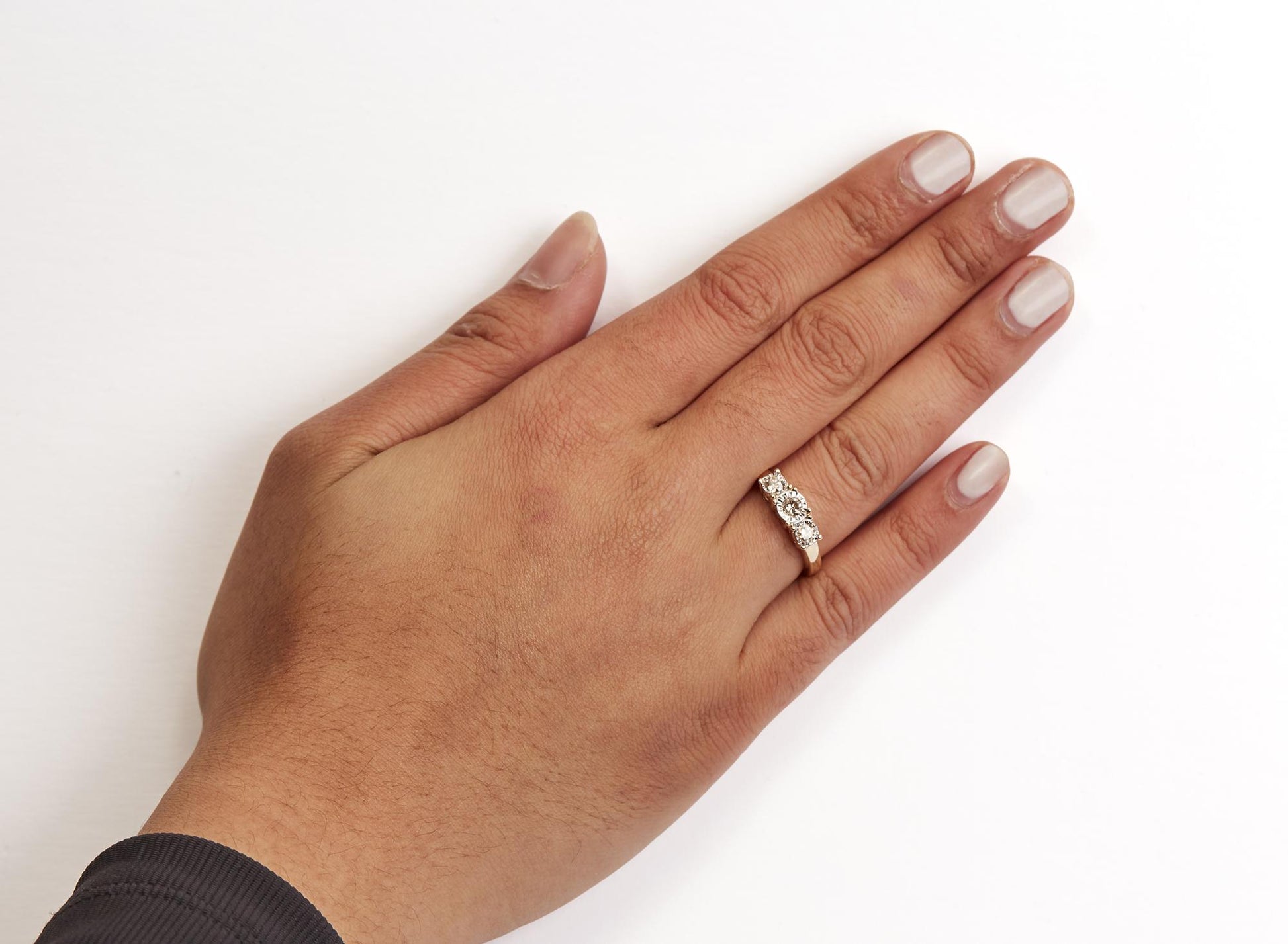 Yellow metal ring with three round white gemstones in miracle setting, shown on a model hand from top angle.