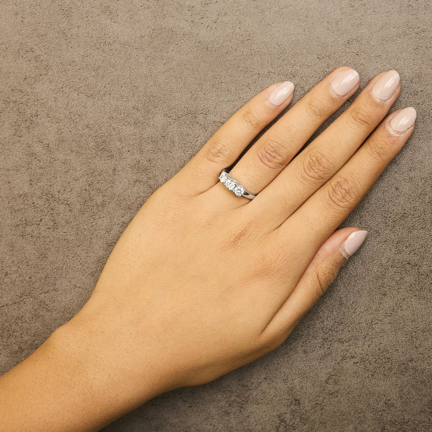 White metal ring with three round white gemstones in four-prong settings, shown on a model's hand from a top angle.
