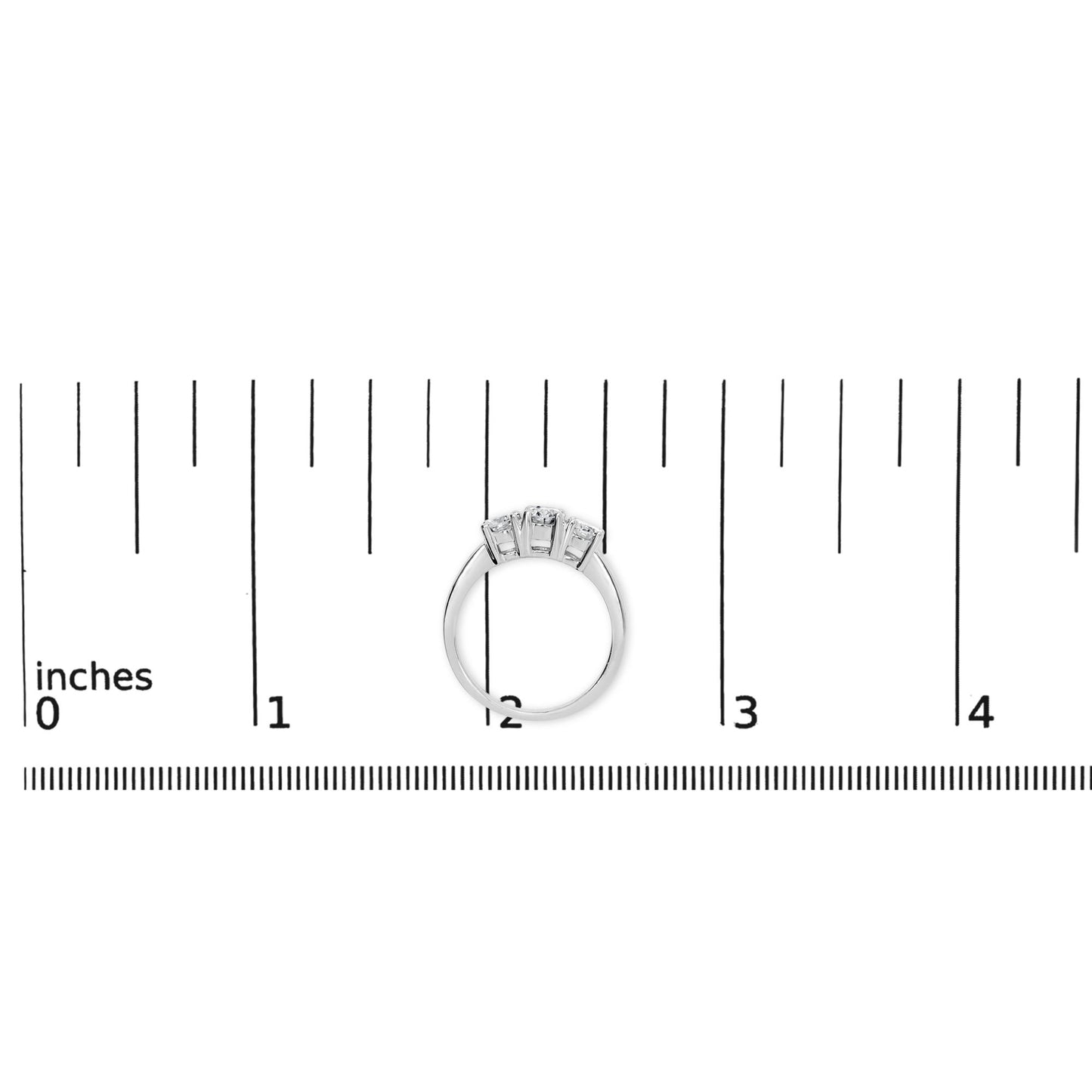 Top view of a white ring with three round white gemstones in four-prong settings, placed on a ruler for size reference.
