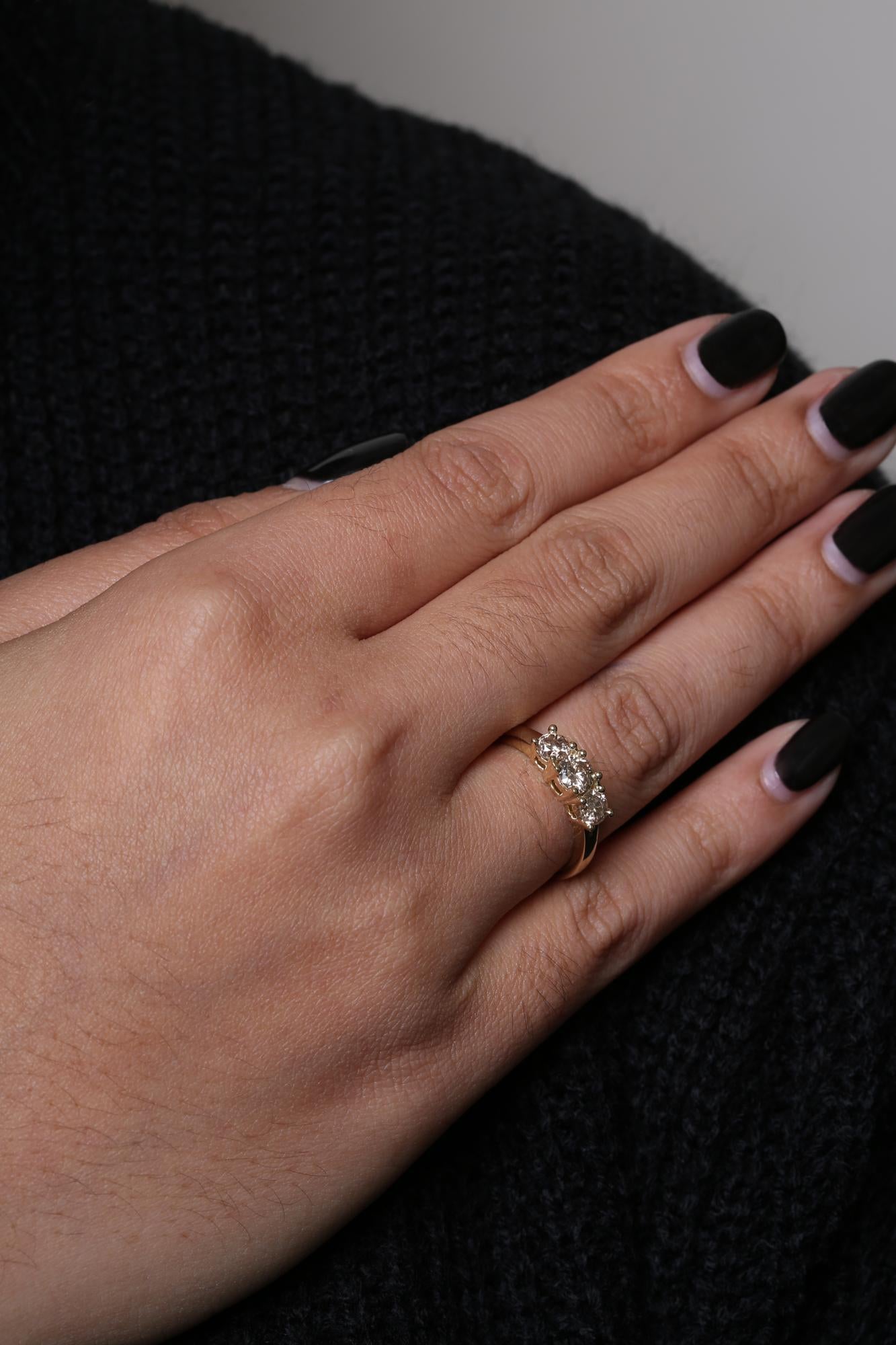 Yellow metal ring with three round white gemstones in prong settings, shown worn on a model's hand from a top angle.