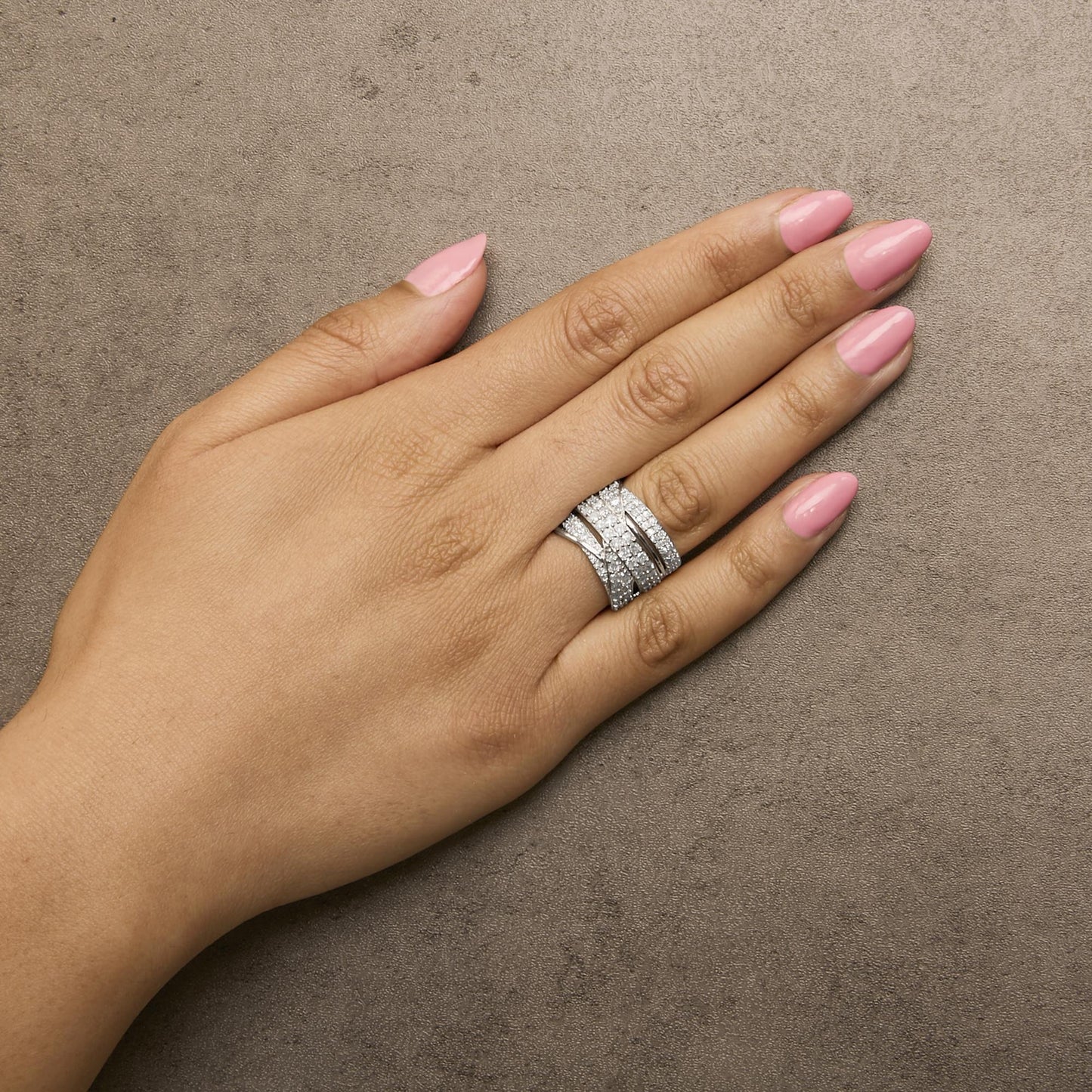 White metal ring with multiple rows of round white gemstones in prong settings, shown on a model's hand from a top angled view.