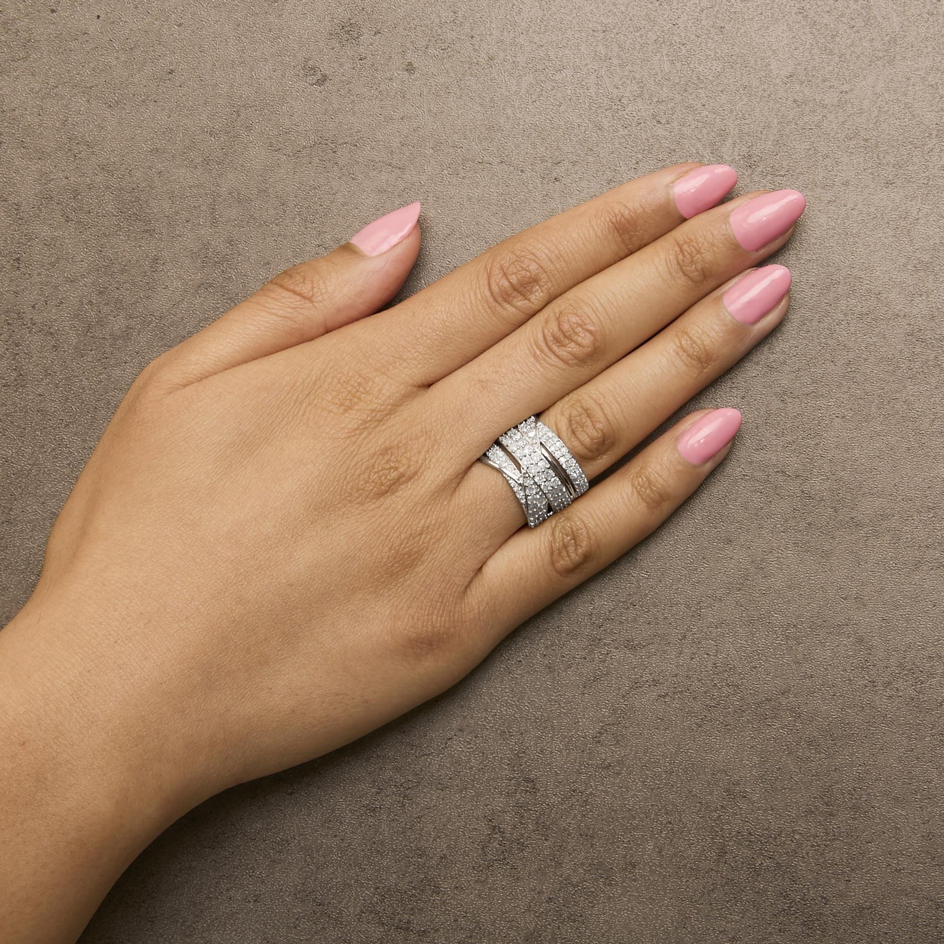White metal ring with multiple rows of round white gemstones in prong settings, shown on a model's hand from a top angled view.