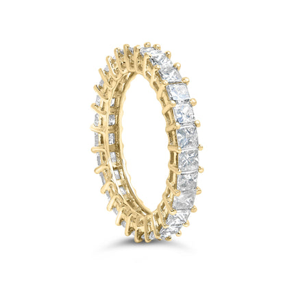 Yellow metal eternity ring with prong-set white princess shape gemstones, shown at a slight angle.