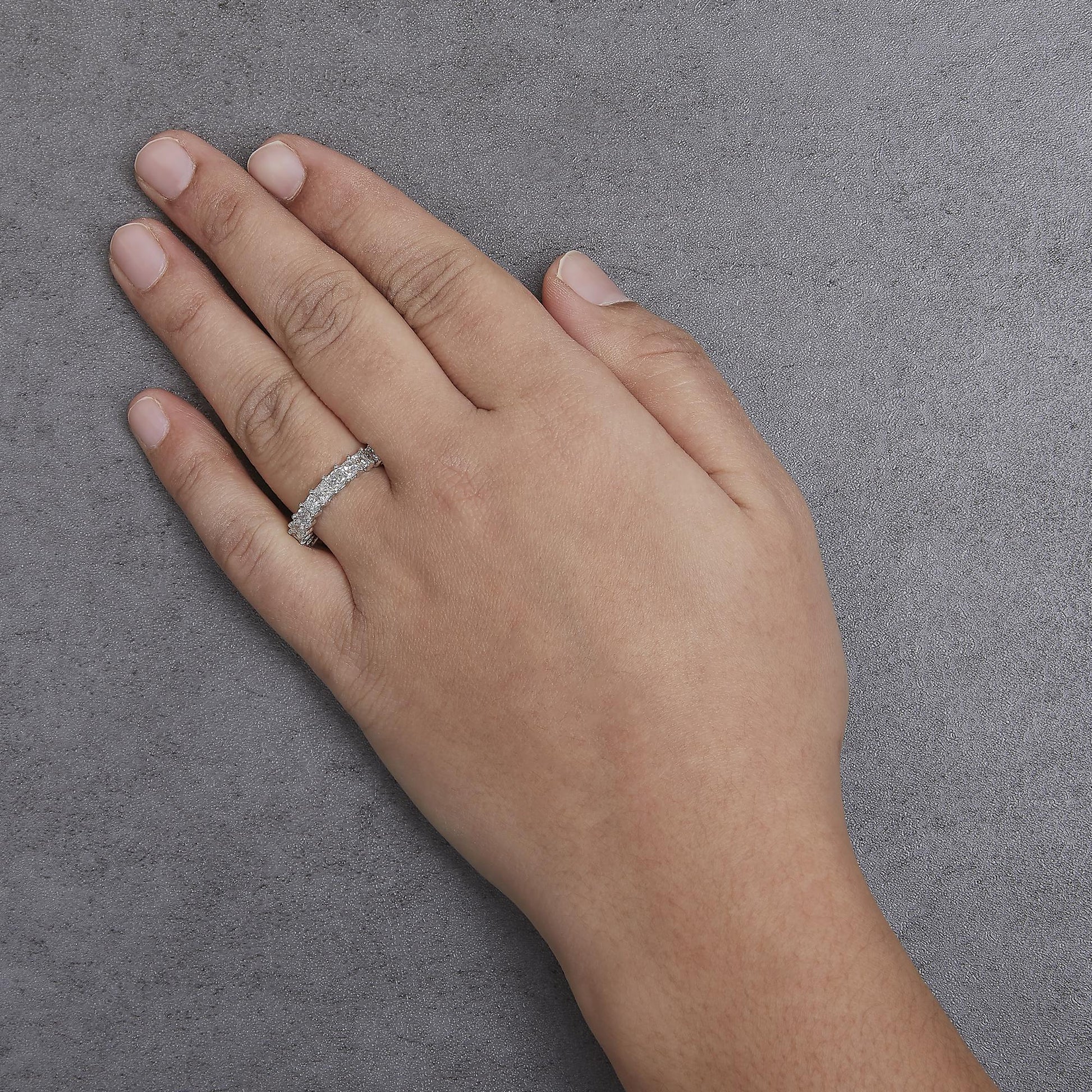 White metal ring with princess-shaped white gemstones in shared prong setting on a model's hand, angled top-down.