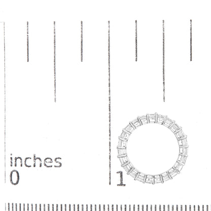 Top-down view of a white metal ring with multiple princess-shaped white gemstones in a shared prong setting, placed on a ruler for size reference.