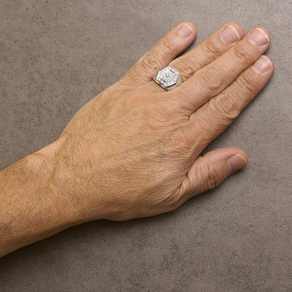 White metal ring with a hexagonal face featuring a central round white gemstone surrounded by multiple smaller round white gemstones, worn on a model's hand, top-down angle.