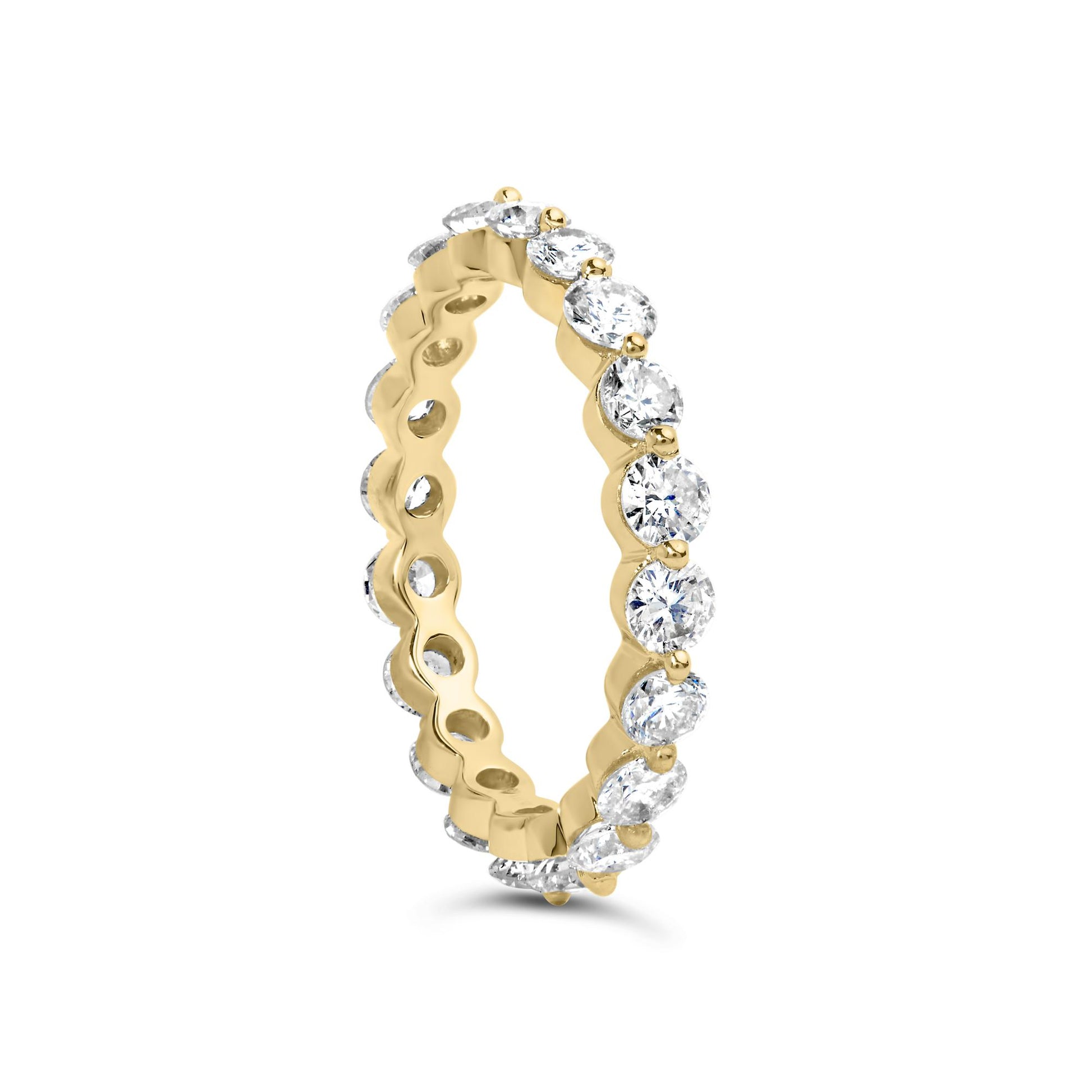Yellow metal eternity ring with round white gemstones in prong settings, shown at a slight angle.