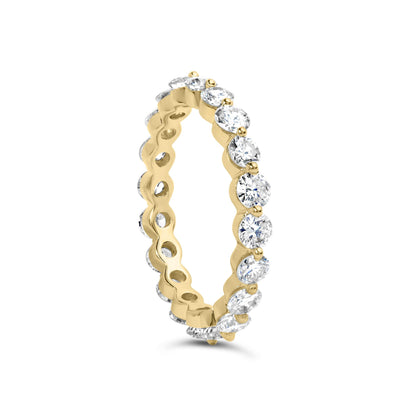 Yellow metal eternity ring with round white gemstones in prong settings, shown at a slight angle.