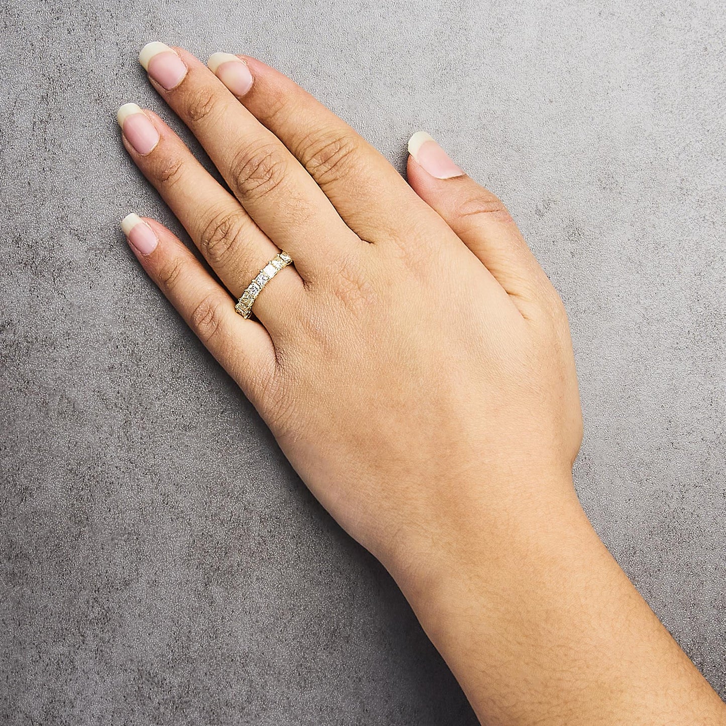 Close-up of a hand wearing a yellow ring with prong-set white princess-shaped gemstones, shown from a top angle.