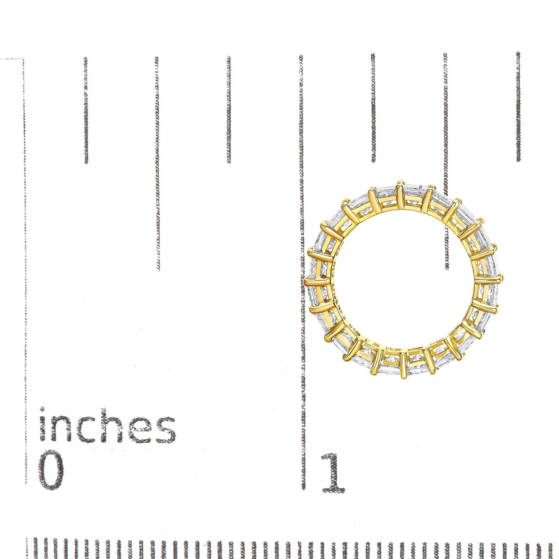 Top-down view of a yellow metal ring with white princess-shaped gemstones in a prong setting, placed on a ruler for size reference.