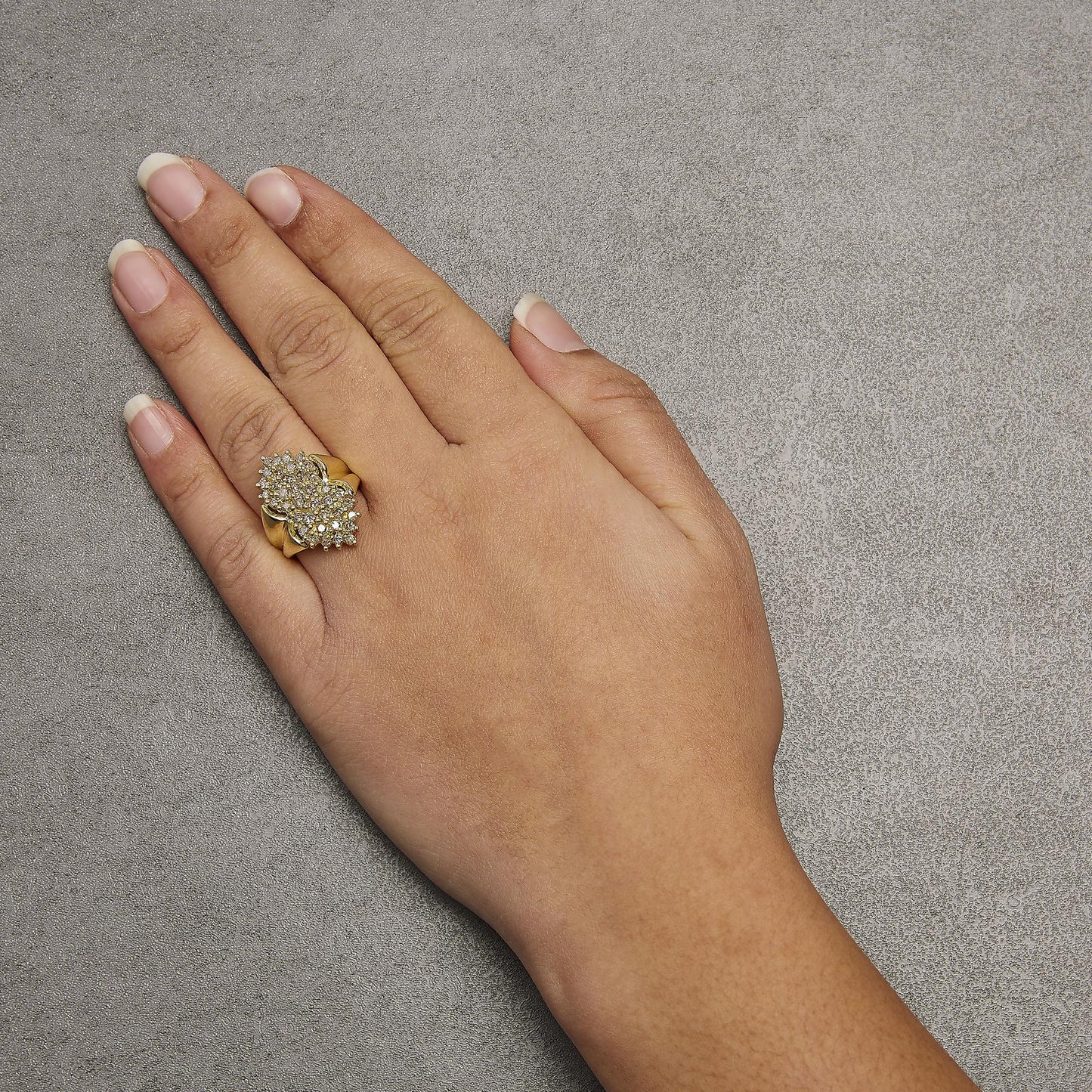 Yellow metal ring with two cluster arrangements of round, prong-set champagne-colored gemstones, worn on a model's hand, shown from a top angle.