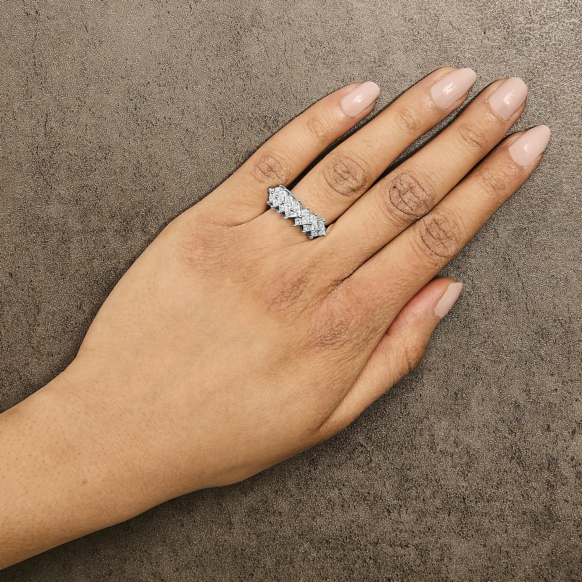 Close-up front angle of a model's hand wearing a white metal ring featuring an alternating pattern of princess-shaped white gemstones in an invisible setting.