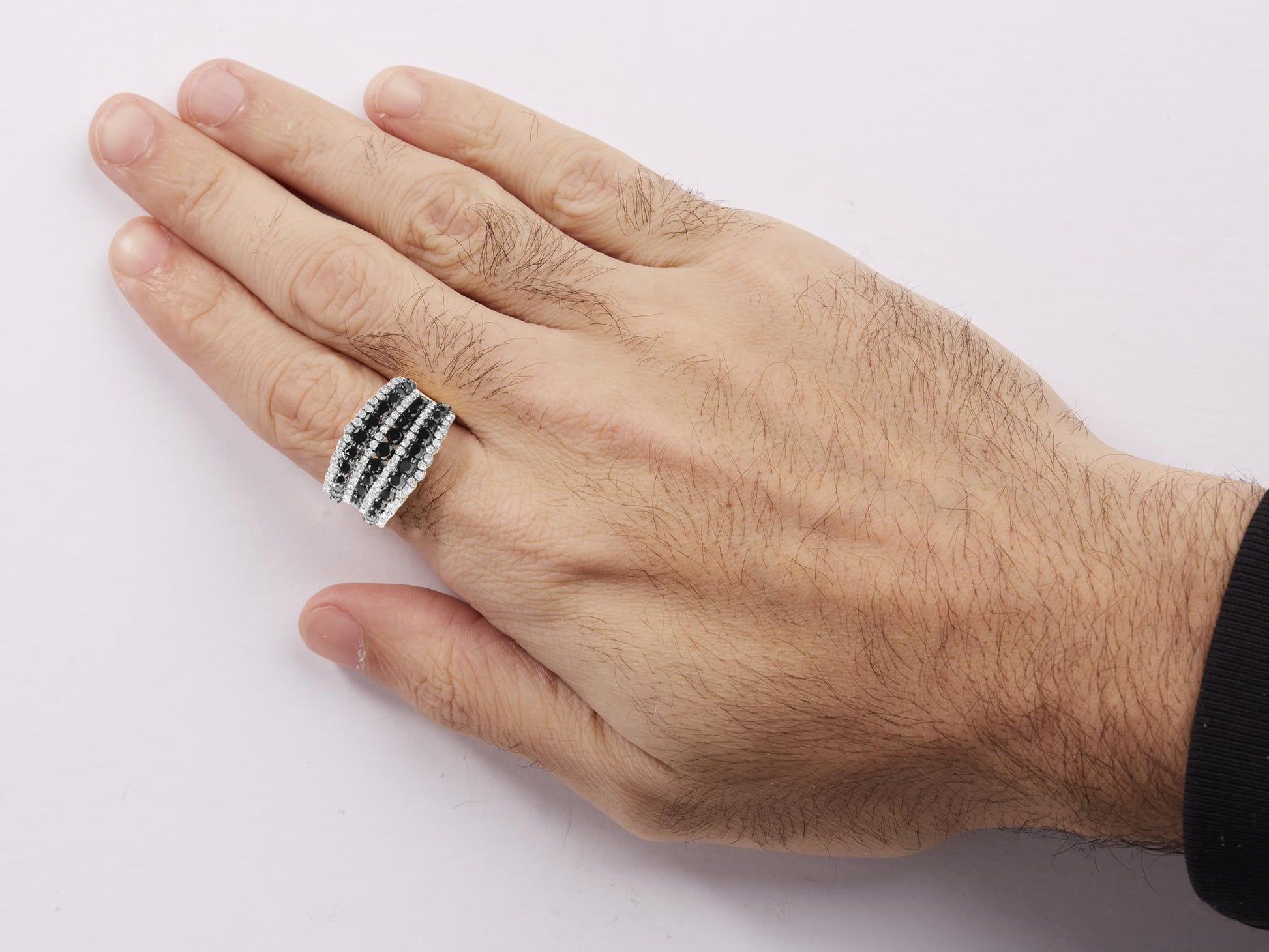 Close-up angled top view of a hand wearing a white metal ring with multiple rows of round black and white gemstones in prong settings.