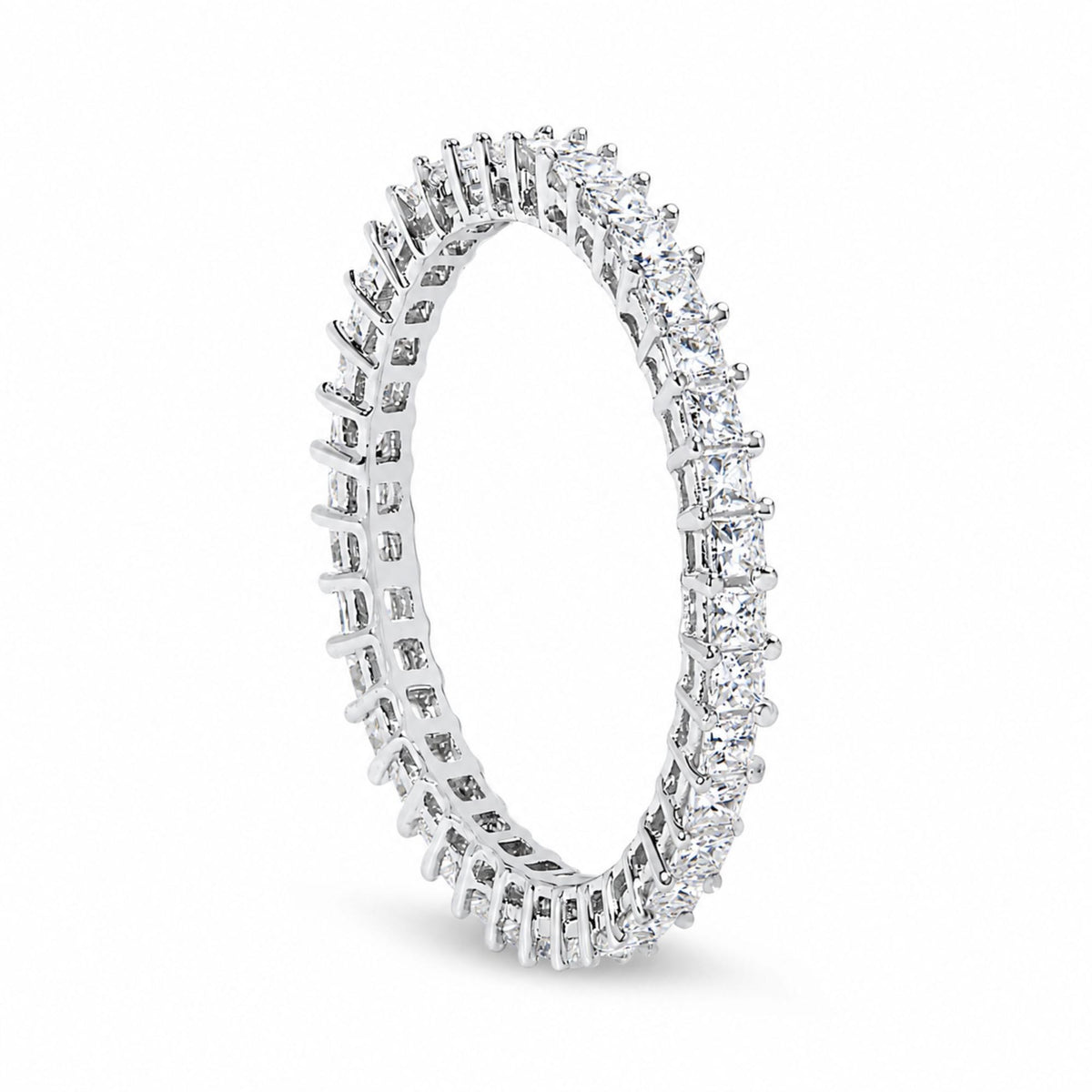 Close-up front angled shot of a white metal ring featuring princess shape white gemstones in prong settings encircling the entire band.