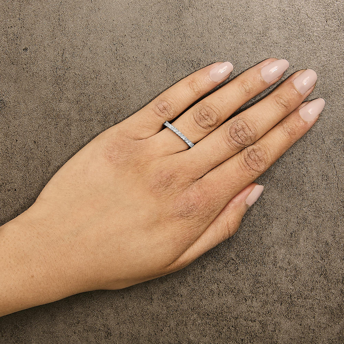 Close-up side angle of a model's hand wearing a white ring featuring princess-shaped white gemstones in a prong setting all around the band.