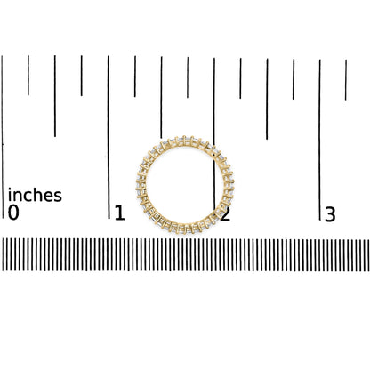 Top-down view of a yellow ring with a continuous row of white princess-shaped gemstones in prong settings, shown on a scale background.