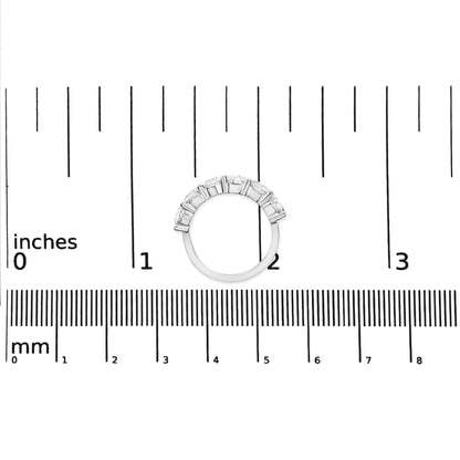 Top-down view of a white metal ring with round white gemstones in a shared prong setting, placed on a ruler for size reference.