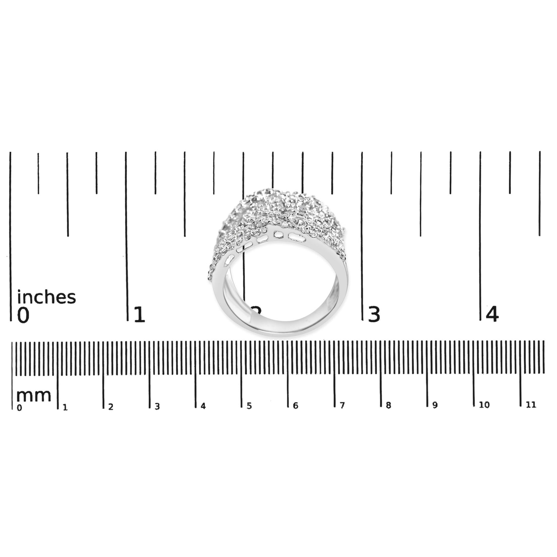 White metal ring with princess shape gemstones in an invisible setting and round shape gemstones in prong settings, shown from a slightly tilted side angle on a ruler for size reference.