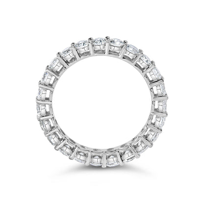 Top-down close-up of a white metal eternity band ring featuring round white gemstones in a shared prong setting encircling the entire band.