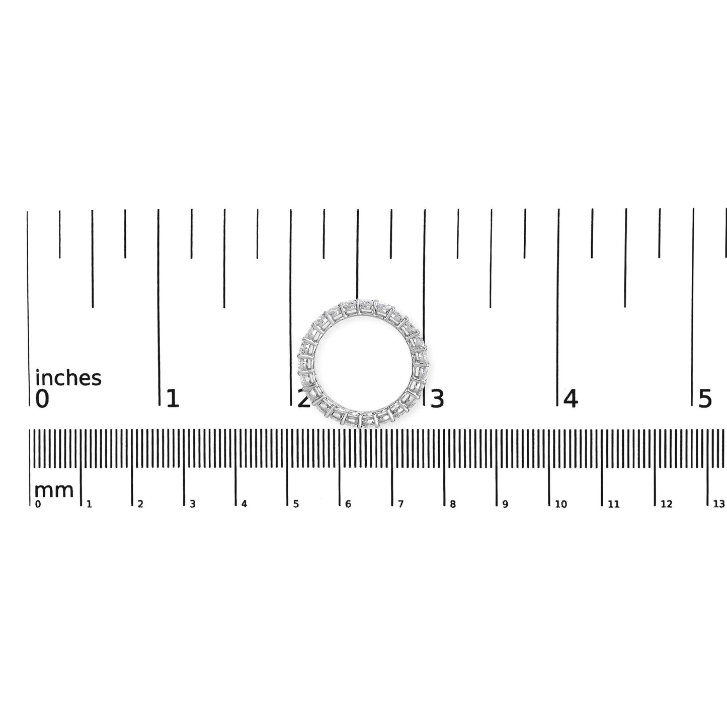 Top-down view of a white ring with round white gemstones in shared prong settings placed on a ruler for size reference.