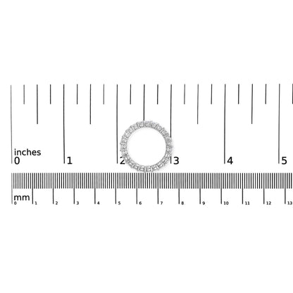 Top-down view of a white ring with round white gemstones in shared prong settings placed on a ruler for size reference.