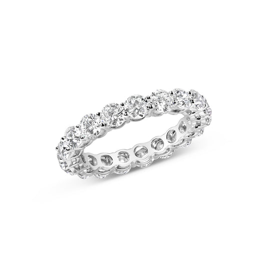 White metal eternity ring with round white gemstones in prong settings, shown at an angle.