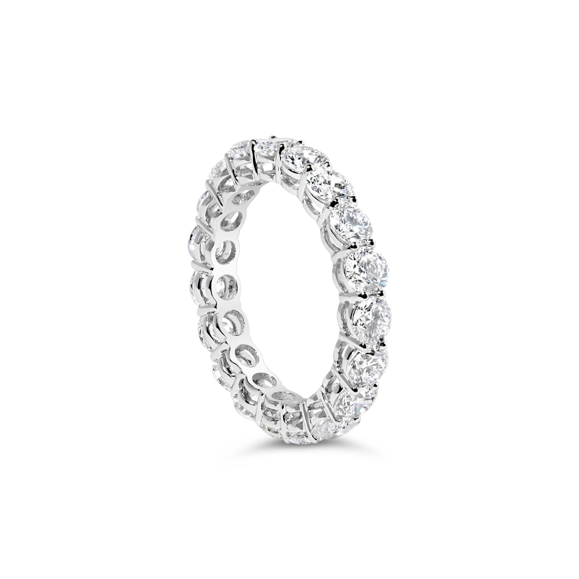 White metal eternity ring with round white gemstones in prong settings, shown from a slightly angled side view.