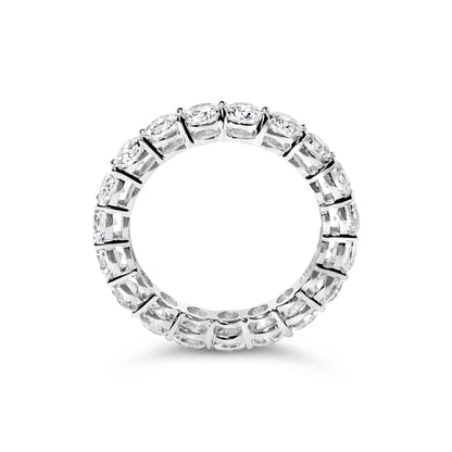 Top-down view of a white ring with round white gemstones set in prong settings encircling the band.