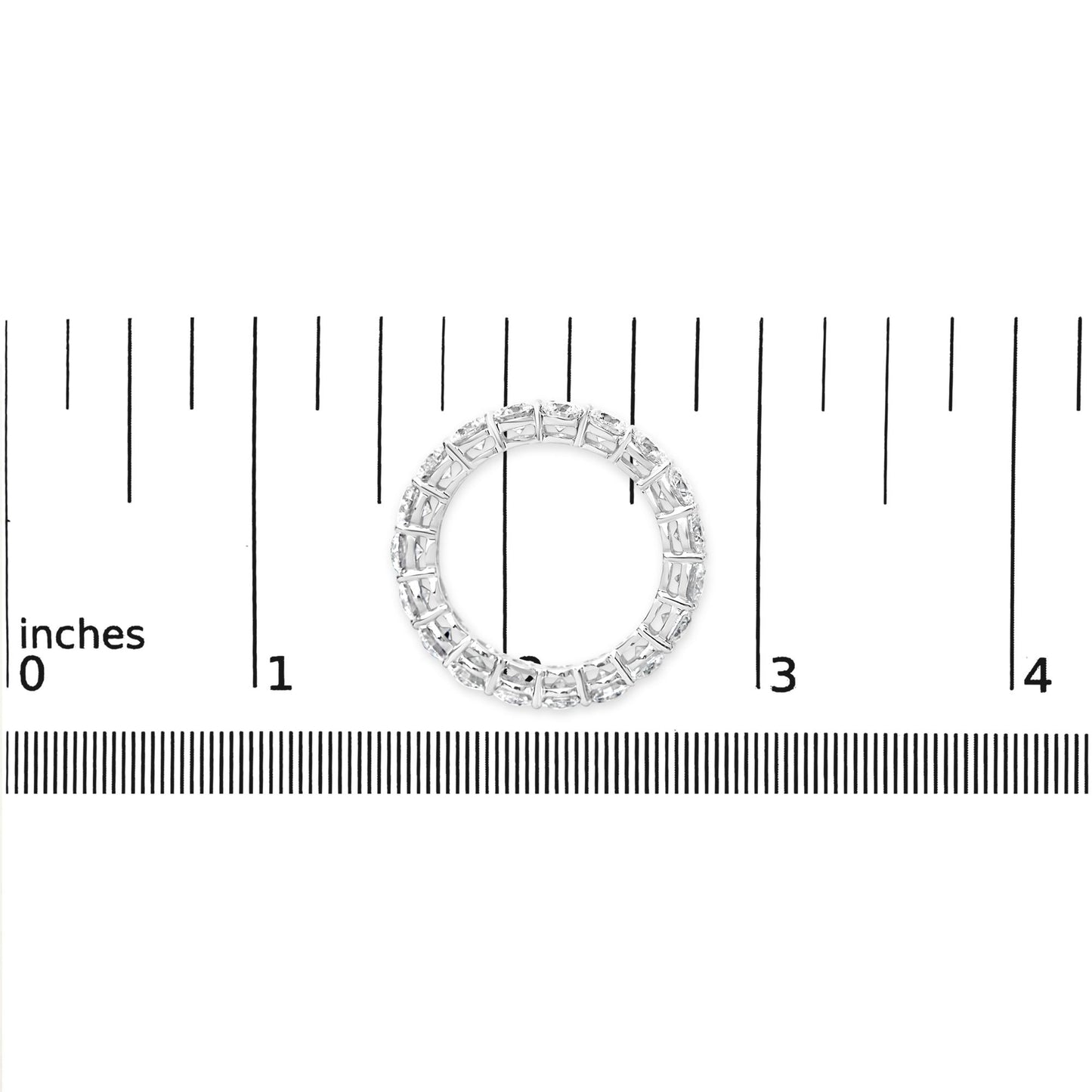 Top view of a white metal ring with round white gemstones in prong settings, placed on a ruler for size reference.