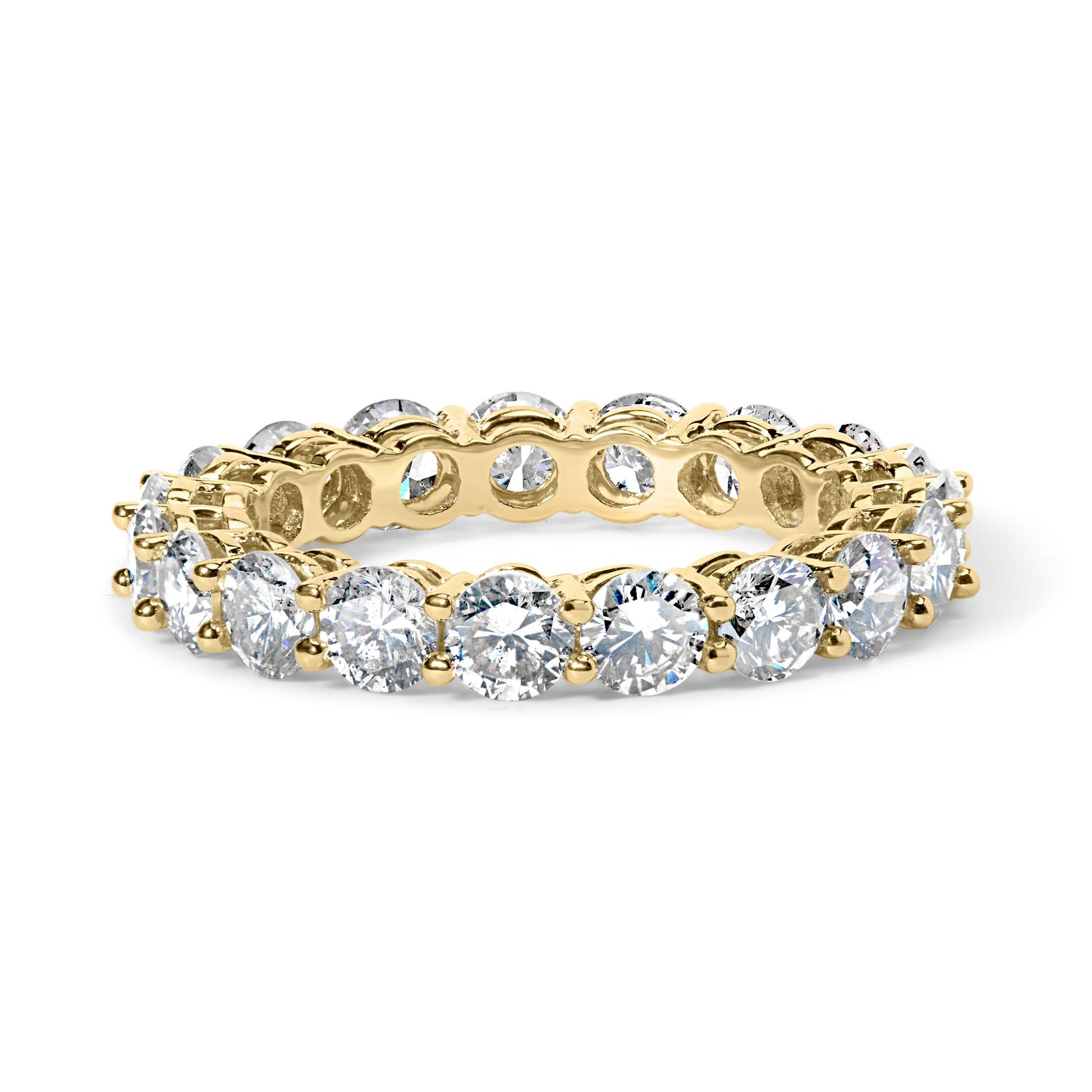 Close-up front angle of a yellow metal ring featuring round white gemstones set in a shared prong setting encircling the entire band.