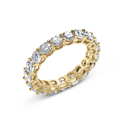 Yellow metal ring with round white gemstones in shared prong setting all around, shown at an angled top view.