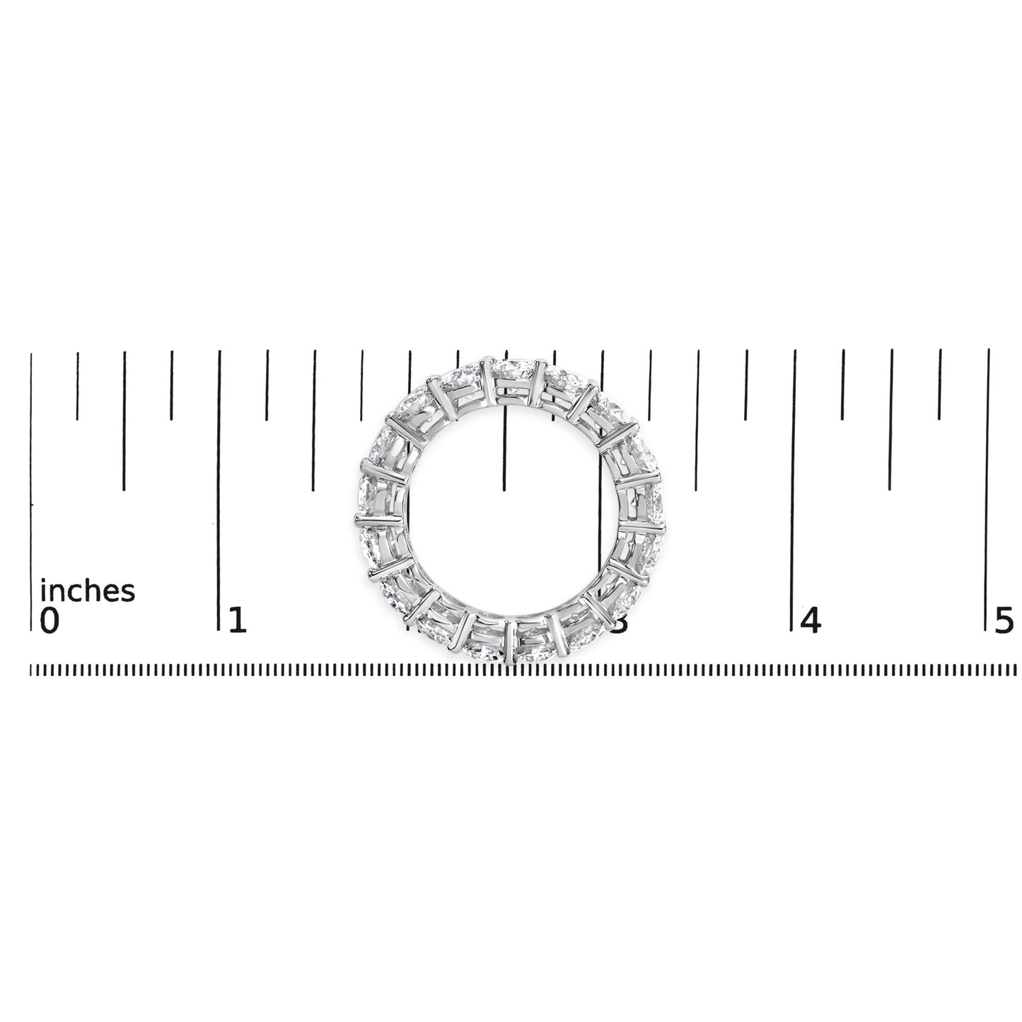 Top-down view of a white metal ring with round white gemstones in a shared prong setting, placed on a ruler for size reference.