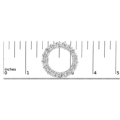 Top-down view of a white metal ring with round white gemstones in a shared prong setting, placed on a ruler for size reference.