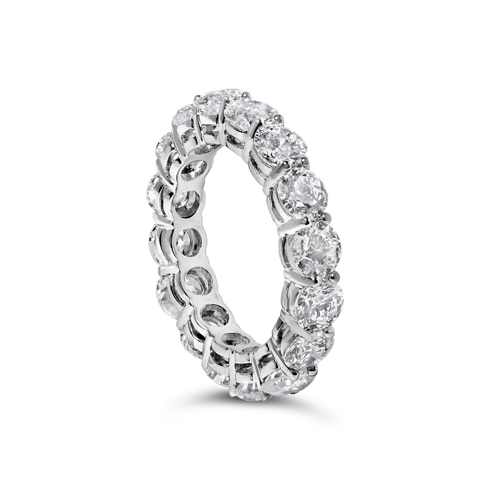White metal eternity ring with round white gemstones in prong settings, shown at an angled close-up.
