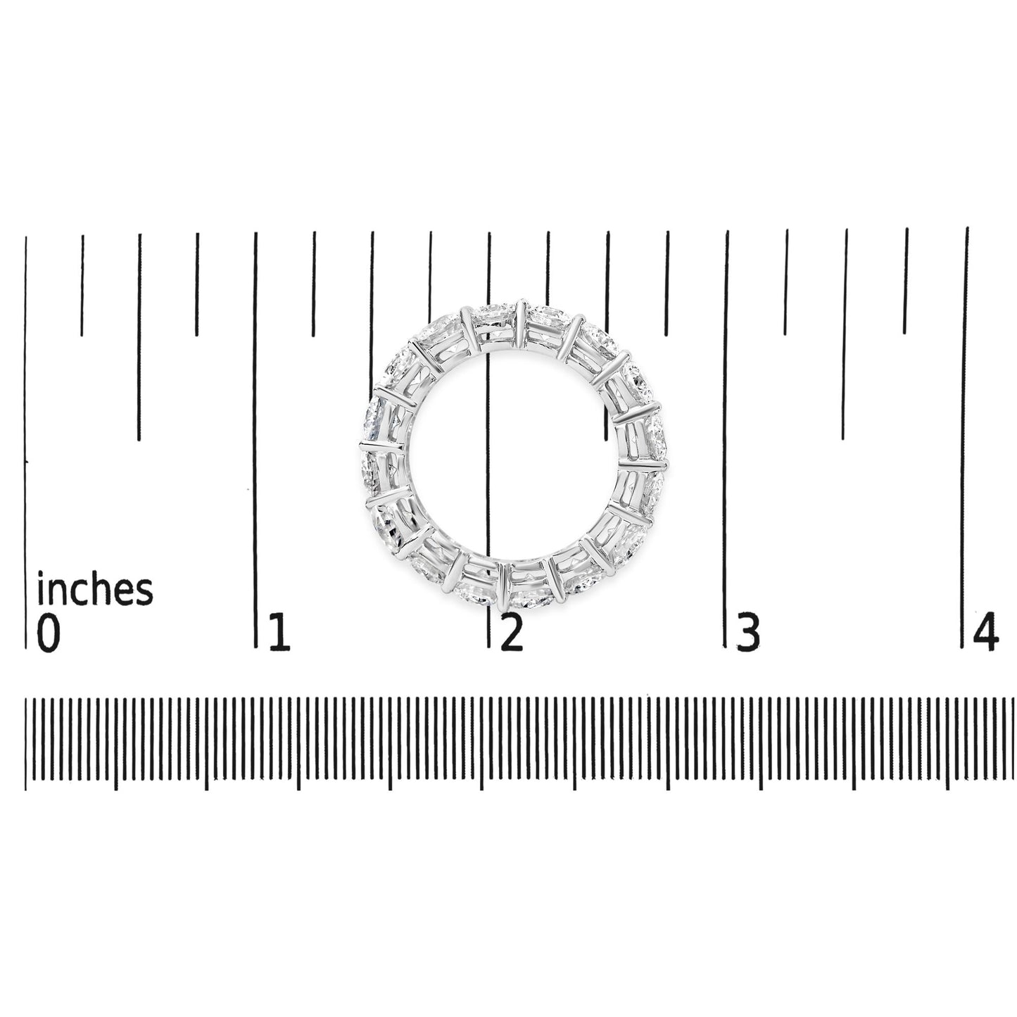 Top-down view of a white metal ring with round white gemstones in prong settings, placed on a ruler for size reference.
