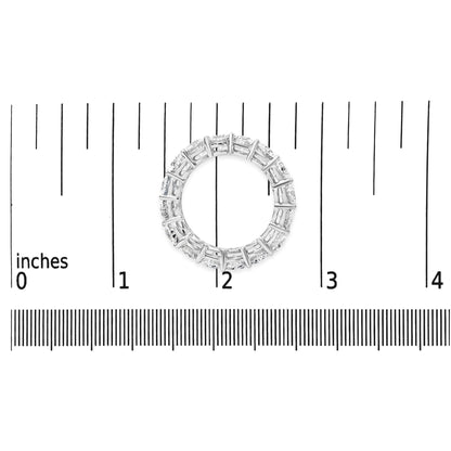 Top-down view of a white metal ring with round white gemstones in prong settings, placed on a ruler for size reference.