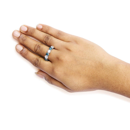White metal ring with alternating round blue and white gemstones in shared prong settings, shown on a model's hand from above at an angle.