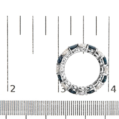 Top-down view of white metal ring with alternating round blue and white gemstones in shared prong setting, placed on a ruler for size reference.