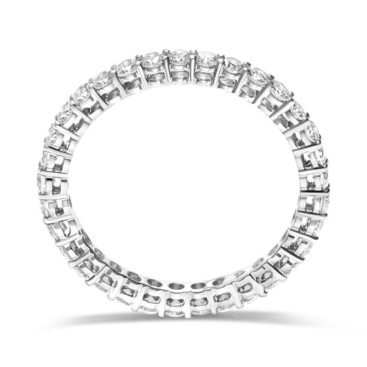 Top-down angled view of a white metal ring featuring round white gemstones set in shared prong settings encircling the entire band.