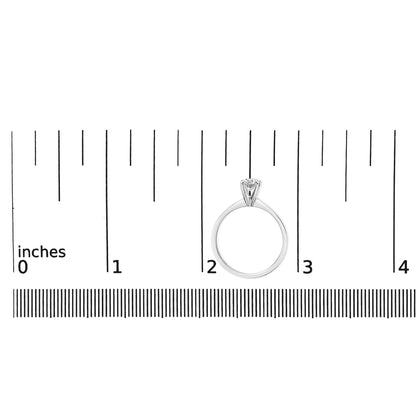 White metal ring with a single round white gemstone in a 4-prong setting, shown upright on a ruler for size reference.